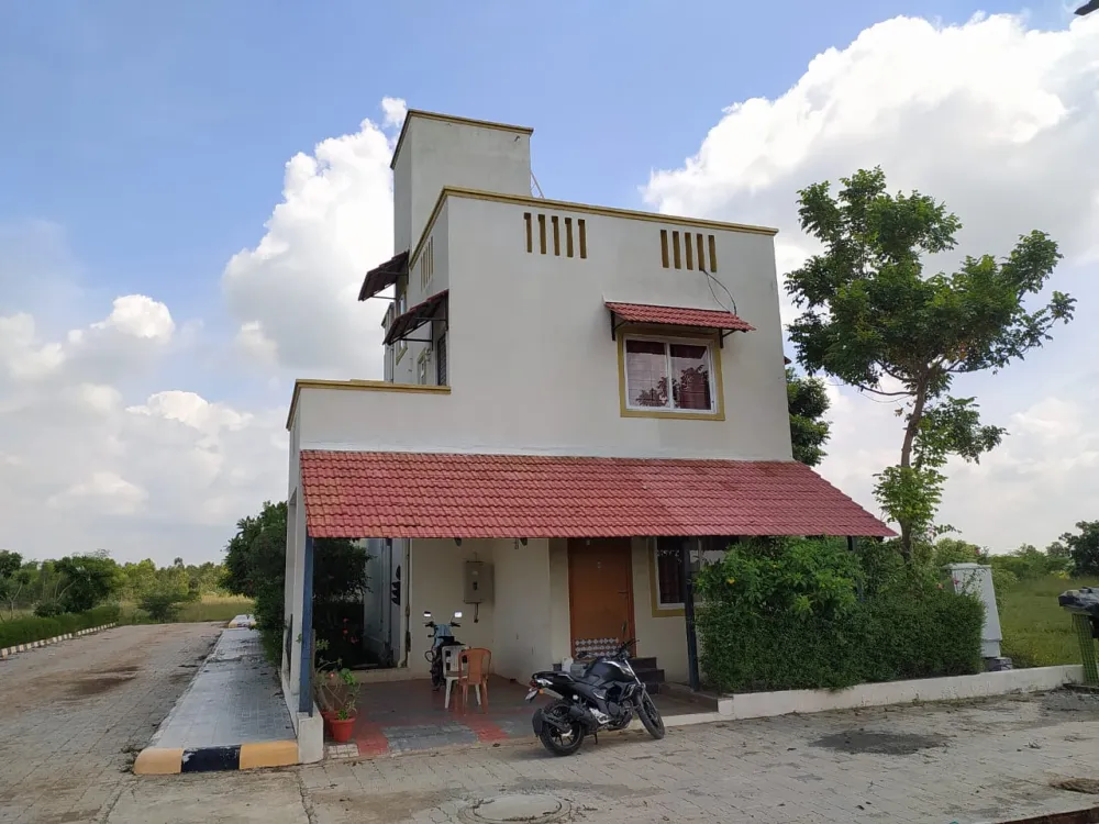 Photograph. A Harmonia duplex villa on its street, lived in: a motorbike under the canopy and chairs by the front door.